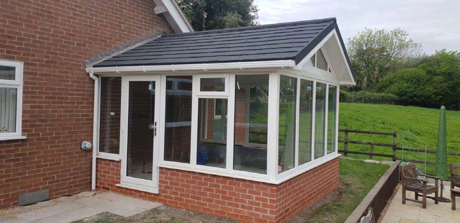 A black tiled roof on a red brick conservatory.